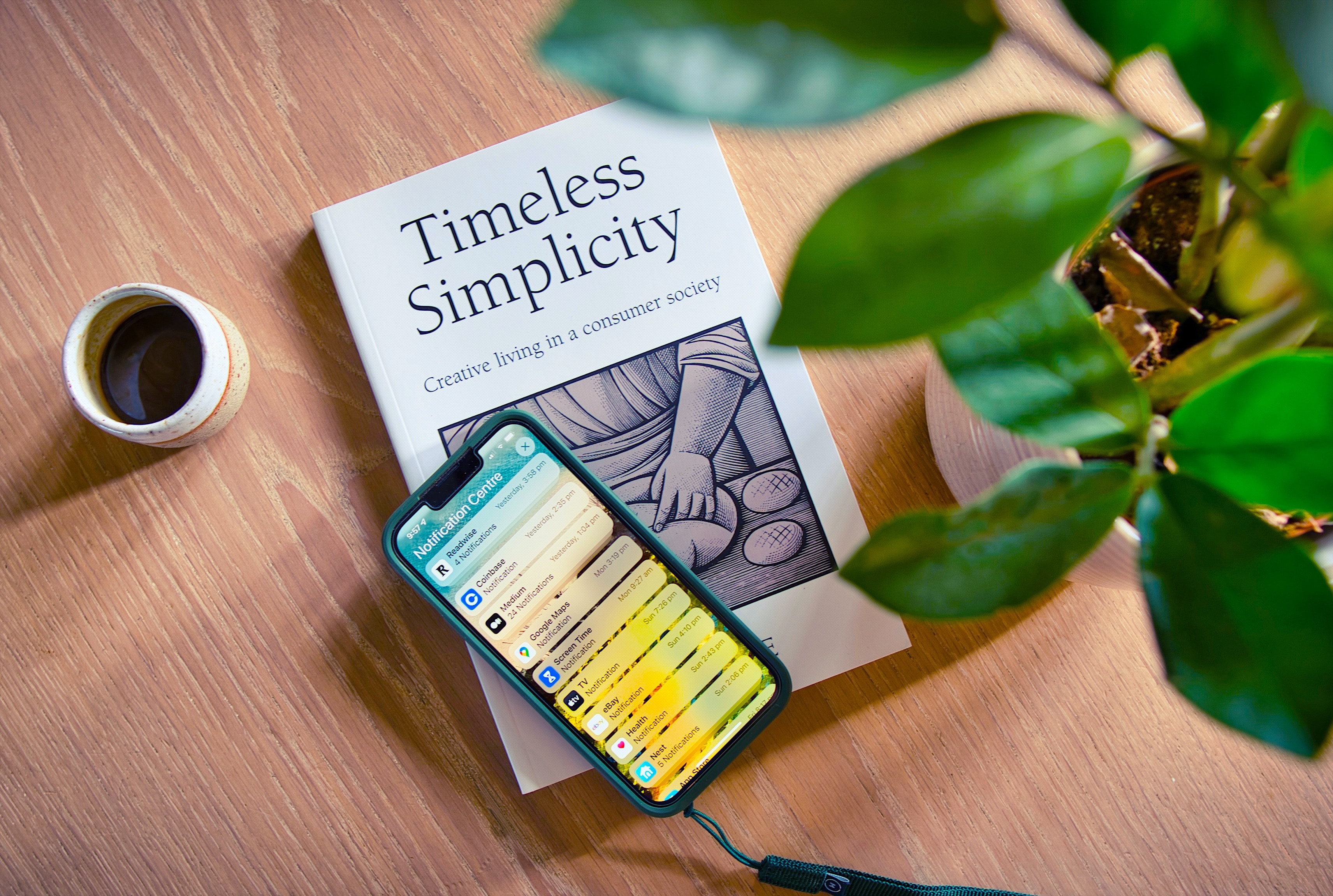 A book titled Timeless Simplicity sits on a desk with a coffee mug, a phone and plant